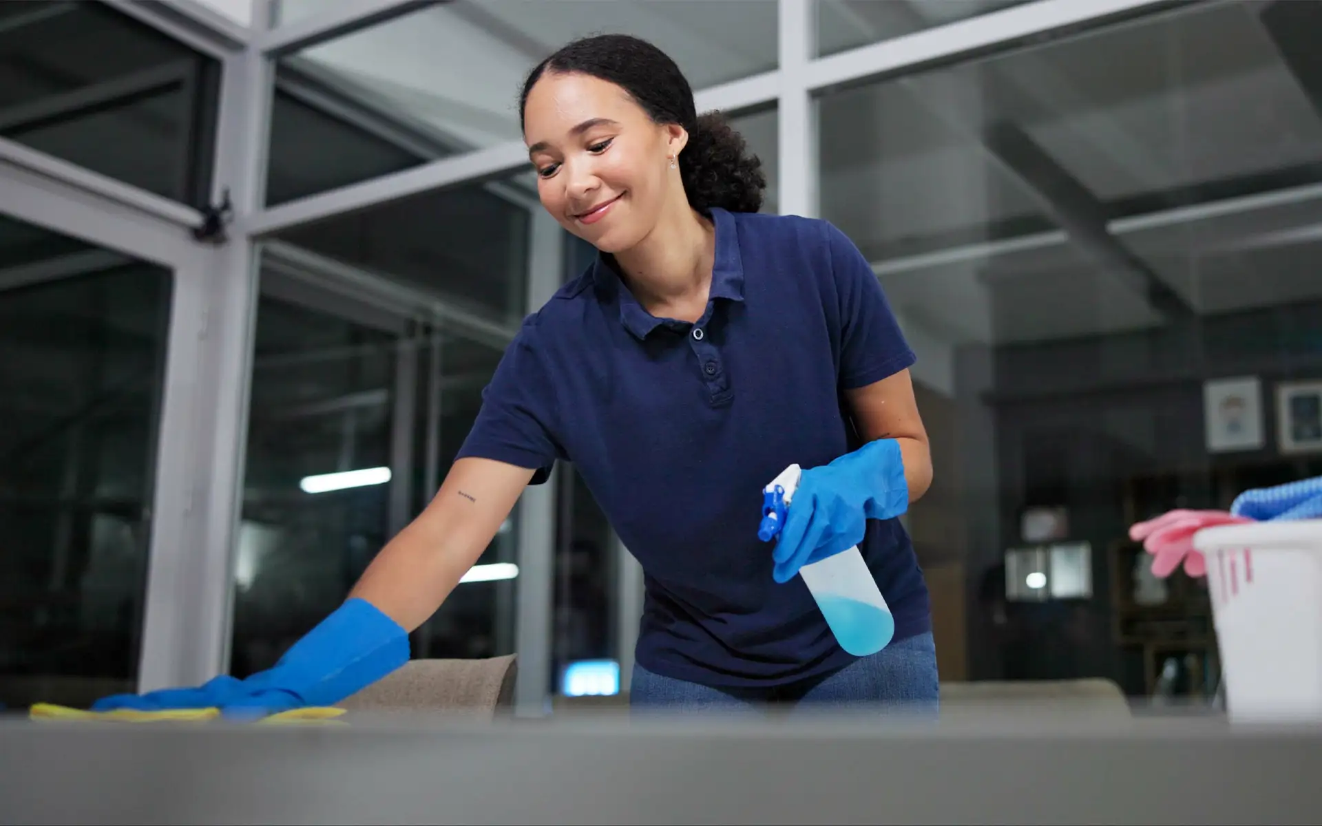 Reinigungskraft reinigt Bürotische von Staub, desinfiziert mit Sprühdesinfektionsmittel und schützt vor Krankheitsrisiken im Gebäude.